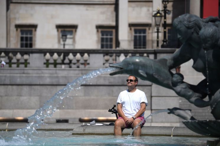 18일(현지시간) 폭염이 덮친 영국 런던에서 한 남성이 트래펄가 광장 분수대에 발을 담근 채 더위를 식히고 있다. [이미지출처=연합뉴스]