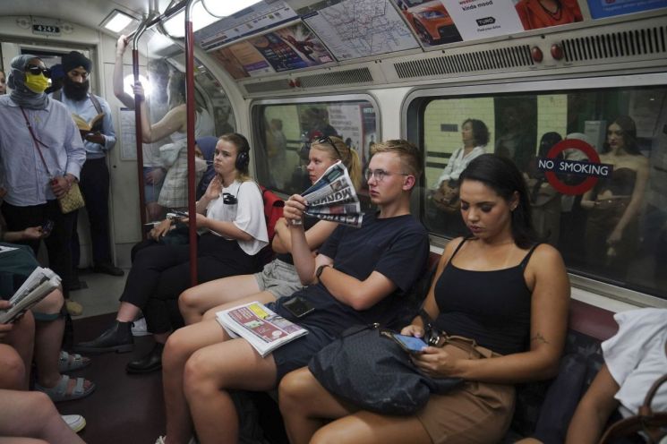 18일(현지시간) 런던 중심부를 지나는 지하철을 이용중인 시민들이 신문지를 부채로 사용하고 있다. [이미지출처=AP연합뉴스]