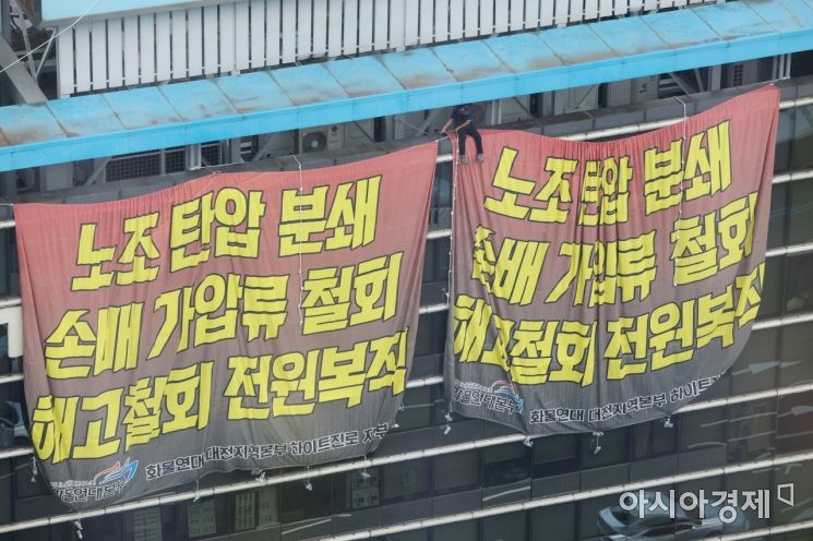 민주노총 공공운수노조 화물연대가 서울 강남구 하이트진로 본사를 점거한 채 사흘째 시위를 이어가고 있는 18일 건물 외벽에 요구사항이 적힌 현수막이 걸려 있다. 노동자가 위태롭게 앉아 있다. /문호남 기자 munonam@