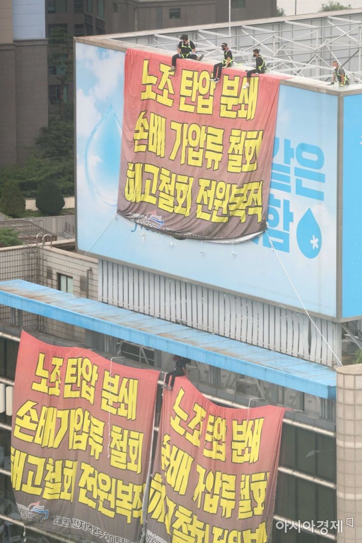 민주노총 공공운수노조 화물연대가 서울 강남구 하이트진로 본사를 점거한 채 사흘째 시위를 이어가고 있는 18일 건물 외벽에 요구사항이 적힌 현수막이 걸려 있다. 노동자들이 옥상 광고판에 올라가 고공 농성을 하고 있다. /문호남 기자 munonam@