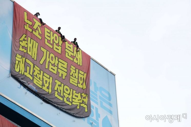 민주노총 공공운수노조 화물연대가 서울 강남구 하이트진로 본사를 점거한 채 사흘째 시위를 이어가고 있는 18일 건물 외벽에 요구사항이 적힌 현수막이 걸려 있다. 노동자들이 옥상 광고판에 올라가 고공 농성을 하고 있다. /문호남 기자 munonam@