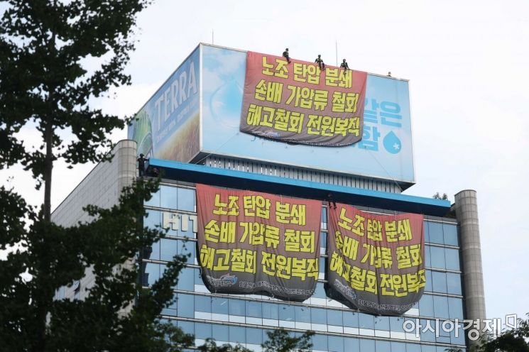 민주노총 공공운수노조 화물연대가 서울 강남구 하이트진로 본사를 점거한 채 사흘째 시위를 이어가고 있는 18일 건물 외벽에 요구사항이 적힌 현수막이 걸려 있다. 노동자들이 옥상 광고판에 올라가 고공 농성을 하고 있다. /문호남 기자 munonam@