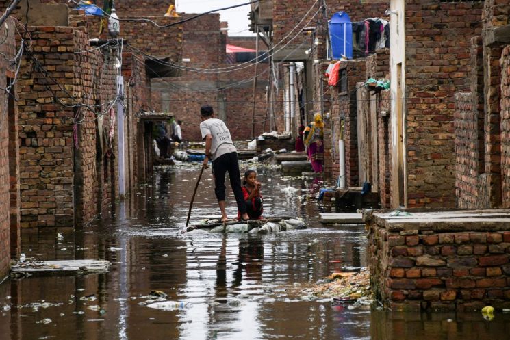 지난달 24일(현지시간) 몬순 폭우가 쏟아진 파키스탄 남부 신드주 하이데라바드에서 한 남성과 소녀가 뗏목을 타고 침수된 거리를 지나고 있다. [이미지출처=연합뉴스]