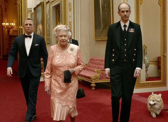 배우 대니얼 크레이그(왼쪽)가 2012 런던 올림픽 개막식에서 엘리자베스 2세(가운데) 여왕을 호위하고 있는 모습. 반려견 코기가 이를 뒤따르고 있다. 사진=AFP 연합뉴스