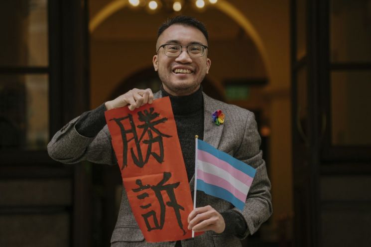 홍콩의 트랜스젠더 활동가 헨리 에드워드 쯔가 6일 최고법원인 종심법원 앞에서 트랜스젠더를 상징하는 깃발과 '승소'라고 적힌 종이를 들고 활짝 웃고 있다. [이미지출처=AP연합뉴스]