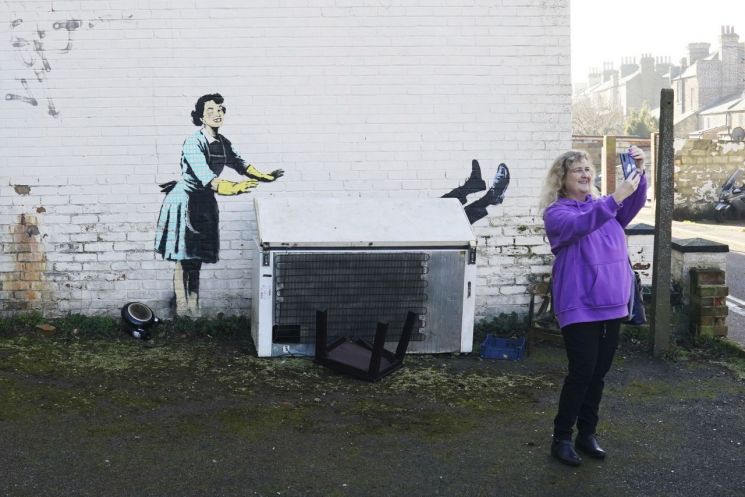 그라피티 작가 뱅크시가 그린 '밸런타인데이 마스카라' 작품 앞에서 한 시민이 사진을 찍고 있다. [이미지출처=AP연합뉴스]