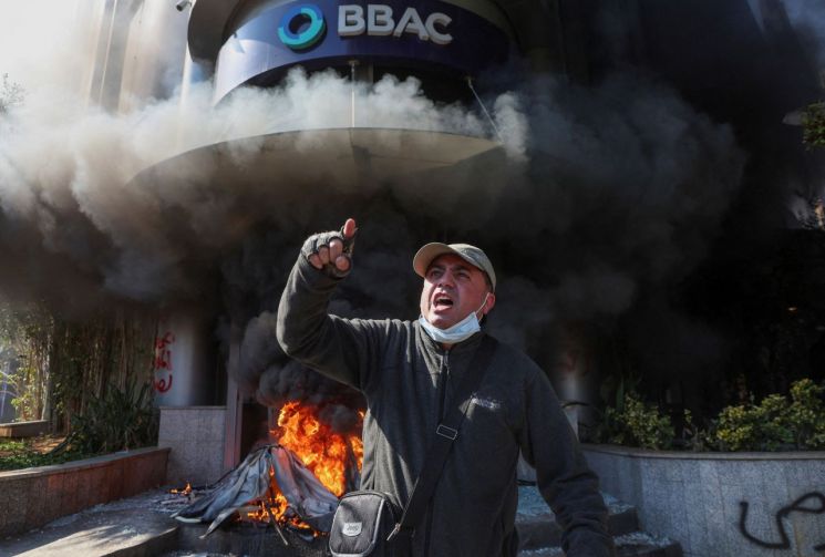 16일(현지시간) 레바논 수도 베이루트의 한 은행 앞에 불이 난 가운데 성난 예금주가 예금 인출 제한에 반발하고 있다. [사진출처=로이터 연합뉴스]
