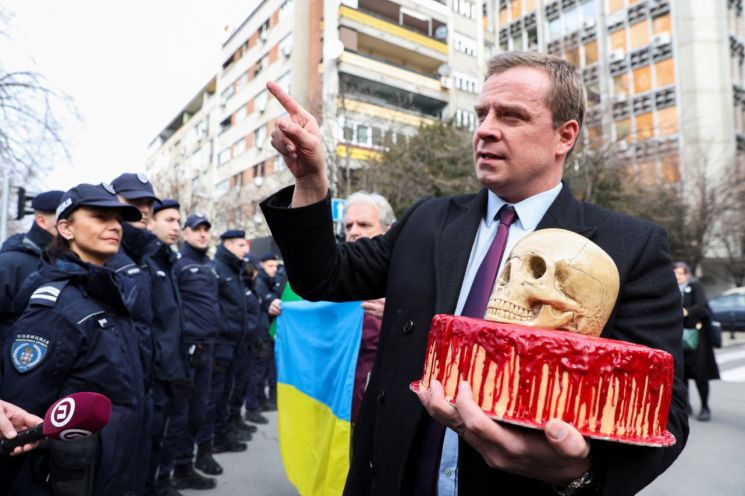24일(현지시간) 세르비아 소재 러시안 대사관 앞에서 한 시위 참가자가 해골이 놓인 핏빛 케이크를 들고 있다.[사진출처=로이터 연합뉴스]