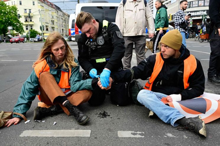 독일 경찰이 지난달 25일(현지시간) 수도 베를린에서 기후운동단체 '마지막 세대'(Letzte Generation) 소속 활동가들의 손에 붙은 접착제를 떼어내고 있다. [사진=베를린 AFP/연합뉴스]