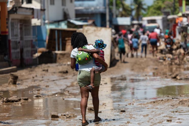 카리브해 섬나라 아이티에서 6일(현지 시각) 한 시민이 아이를 안고 폭우로 진흙탕이 된 거리를 지나가고 있다. 지난 2~4일 아이티 전국에 내린 폭우로 주요 하천과 강이 범람해 지금까지 51명이 숨지고 140명이 다쳤다. 18명은 아직 실종 상태다. [사진=레오간(아이티) EPA/연합뉴스]