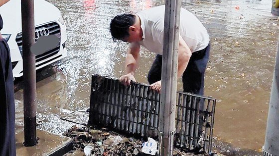 Last August, while a 'water bomb' of 100mm per hour poured down in southern Seoul, a man near Gangnam Station in Seoul is clearing a clogged drainage channel with his bare hands. Photo by online community