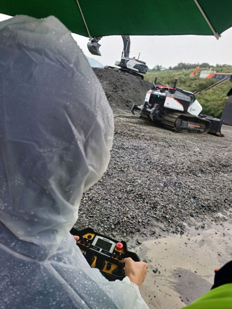 Standing 30 meters away from the 1-ton class DEVELON unmanned dozer by HD Hyundai Site Solutions, operating the dozer with a console (controller) the size of a tablet PC. <br>[Photo by Moon Chae-seok]