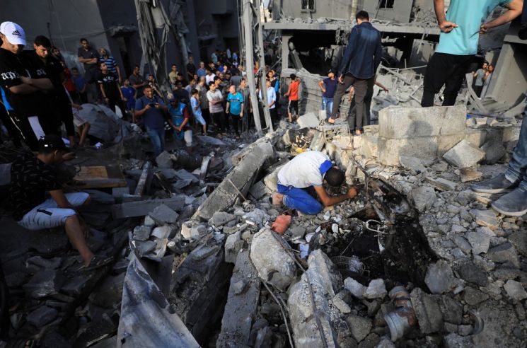 5일(현지시간) 가자지구 알마가지 난민촌에서 주민들이 이스라엘 공습으로 무너진 건물 잔해를 살펴보고 있다. [이미지출처=신화연합뉴스]