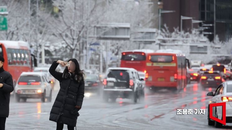 지난해 2월22일 서울 광화문네거리에 출근길에 나선 한 시민이 도심의 눈덮힌 풍경을 휴대폰에 담고 있다. 조용준 기자