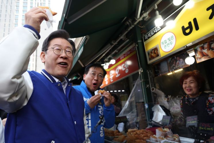 더불어민주당 이재명 대표가 13일 강태웅 후보와 함께 용산구 용문시장을 방문, 상인이 건넨 도너츠를 먹고 있다. [이미지출처=연합뉴스]