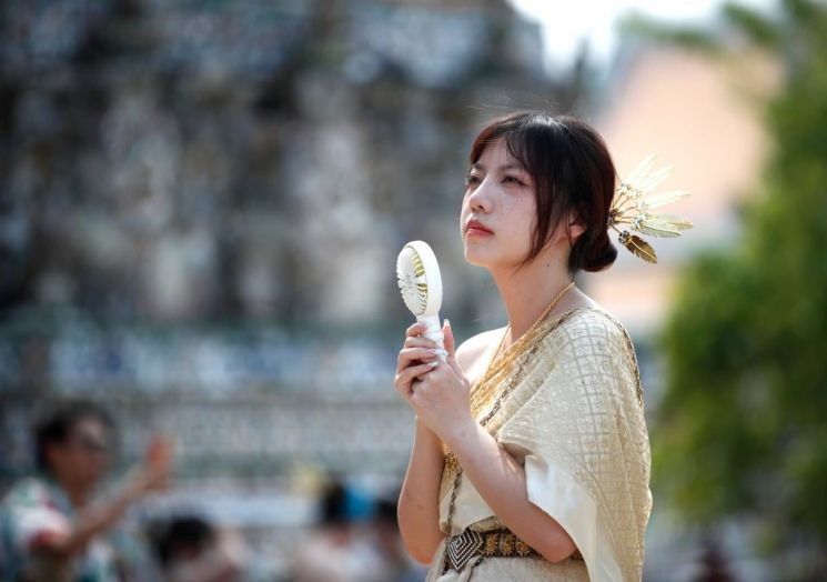 태국 방콕의 관광명소인 왓 아룬 불교사원을 찾은 중국인 관광객이 손 선풍기로 더위를 식히고 있다. [사진출처=연합뉴스]]