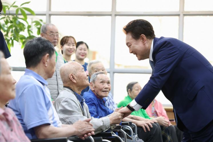 윤석열 대통령이 21일 경기도 수원시 장안구 보훈요양원을 방문해 '나라사랑 액자 만들기' 체험활동 뒤 프로그램에 참여한 참전용사 및 전상·전몰군경 유족 어르신들과 인사하고 있다. [이미지출처=연합뉴스]