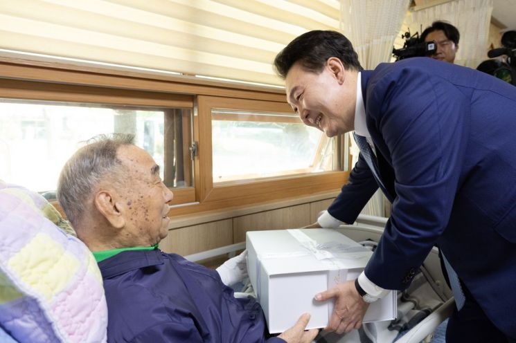 윤석열 대통령이 21일 경기도 수원시 장안구 보훈요양원을 방문해 한 국가유공자에게 '영웅의 제복'을 선물하고 있다. [이미지출처=연합뉴스]