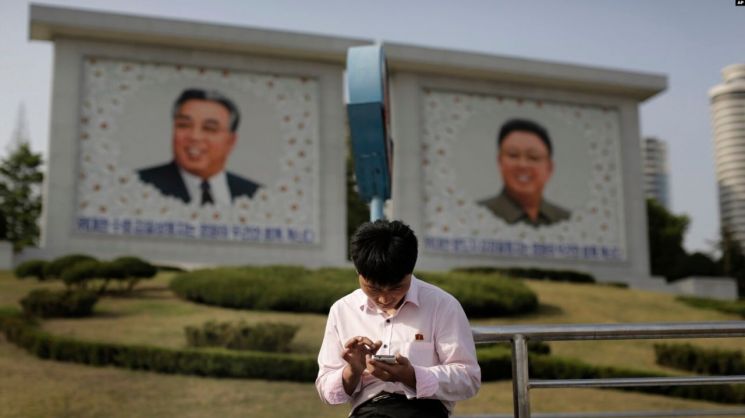 북한 평양의 김일성·김정일 초상화 앞에서 한 남성이 스마트폰을 사용하고 있다. [이미지출처=AP연합뉴스]