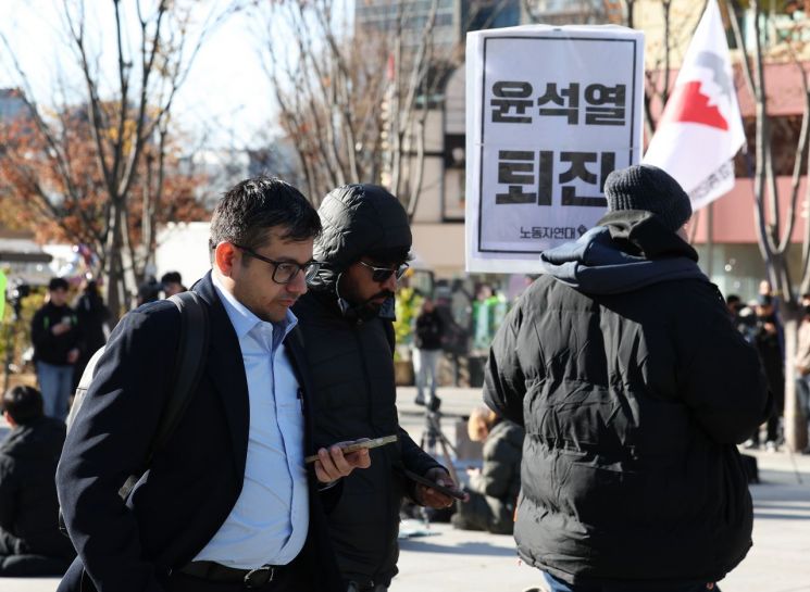 윤석열 대통령이 긴급 대국민 담화를 통해 비상계엄 해제를 선언한 4일 오전 서울 종로구 광화문광장에서 한 외국인 관광객이 계엄 반대 집회를 지나치고 있다. 연합뉴스