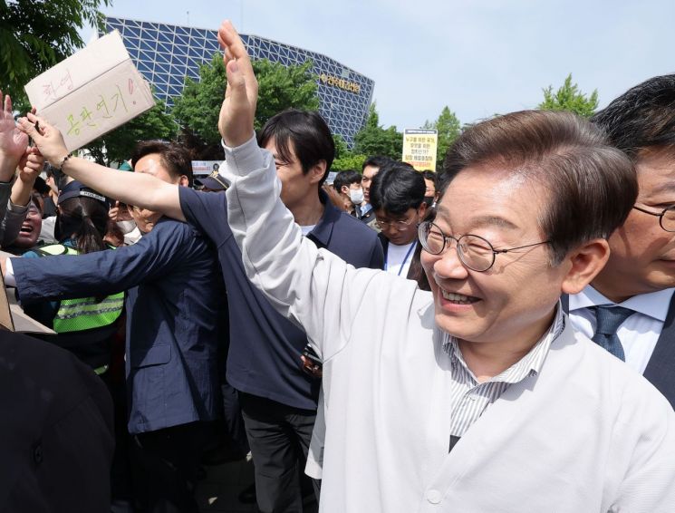 이재명 더불어민주당 대선 후보가 '골목골목 경청투어:국토종주편'에 나선 7일 전북 전주시 풍남문 앞 광장에서 지지자가 든 공판 연기 환영 팻말을 지나고 있다. 이날 서울고등법원은 오는 15일 예정됐던 이 후보의 공직선거법 위반 혐의 사건 파기환송심 첫 공판을 오는 6월 18일로 연기했다. 연합뉴스.