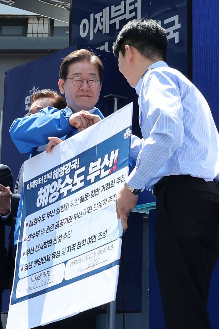 이재명 더불어민주당 대선 후보가 14일 부산 부산진구 서면에서 권기흥 에이치라인해운해상직원노조 위원장과 해양수도 부산 협약서에 서명한 뒤 악수하고 있다. 연합뉴스