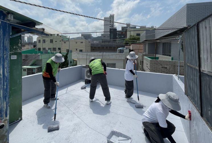 한국주택금융공사 직원들이 대학생 봉사단과 옥상에 열차단 페인트 칠을 하고 있다.