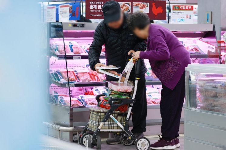 장바구니를 살피는 노부부가 한 대형마트 정육코너에서 식품 가격을 비교하고 있다. 연합뉴스