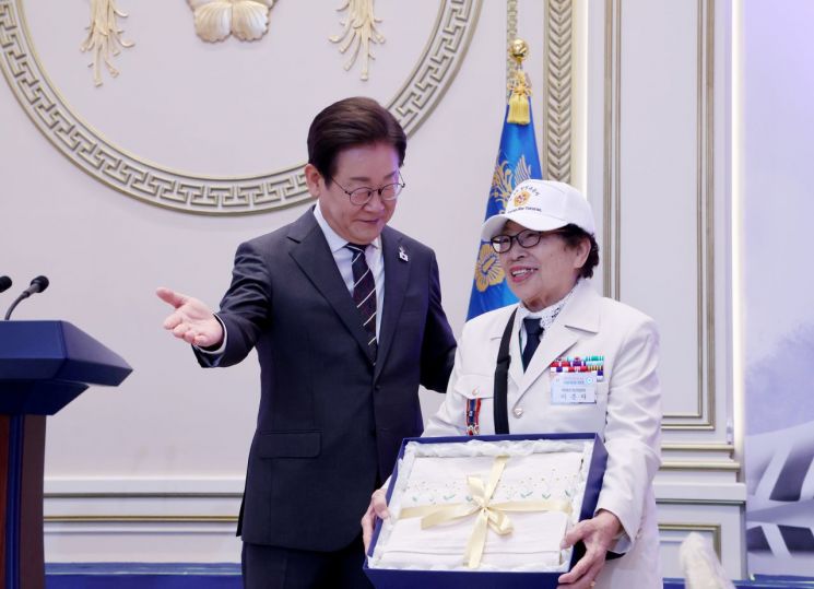 이재명 대통령이 27일 청와대 영빈관에서 열린 '호국 보훈의 달, 대통령의 초대' 행사에서 특별 초청대상자인 이춘자 씨에게 광목이불을 선물하고 있다. 연합뉴스