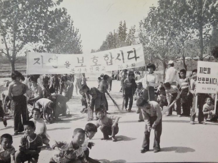 “자연을 보호합시다” 현수막 아래 본량국민학교 학생들이 운동장에서 환경 정화 활동을 하고 있다. 본량초 제공