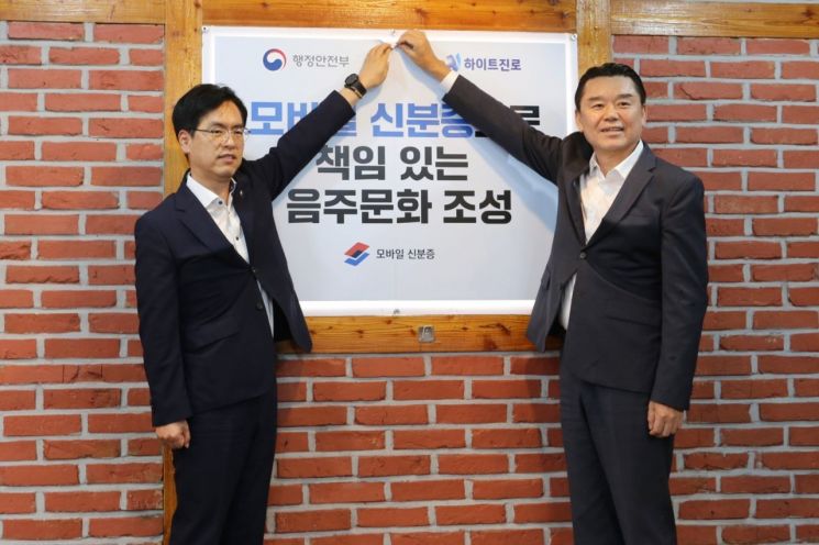 지난 14일 김인규 하이트진로 대표(오른쪽)와 김민재 행정안전부 차관이 행정안전부가 지정한 서울 서초동 하이트진로 본사 인근 착한가격업소를 방문해 모바일 신분증 활용을 권장하는 홍보 포스터를 부착했다.[사진제공=하이트진로]