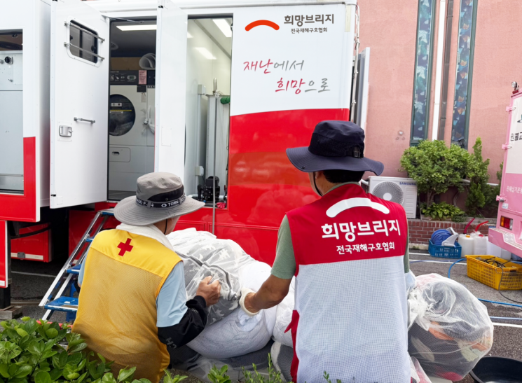 희망브리지 봉사자와 유관기관 봉사자가 세탁차량 앞에서 수해 이웃의 세탁물을 정리하고 있다. 희망브리지