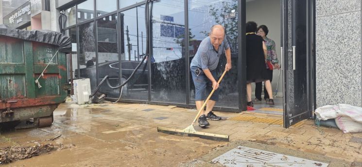 지난 4일 오전 광주 북구 신안동 일대에서 한 상인이 가게 앞 빗물을 쓸어내고 있다. 민찬기 기자
