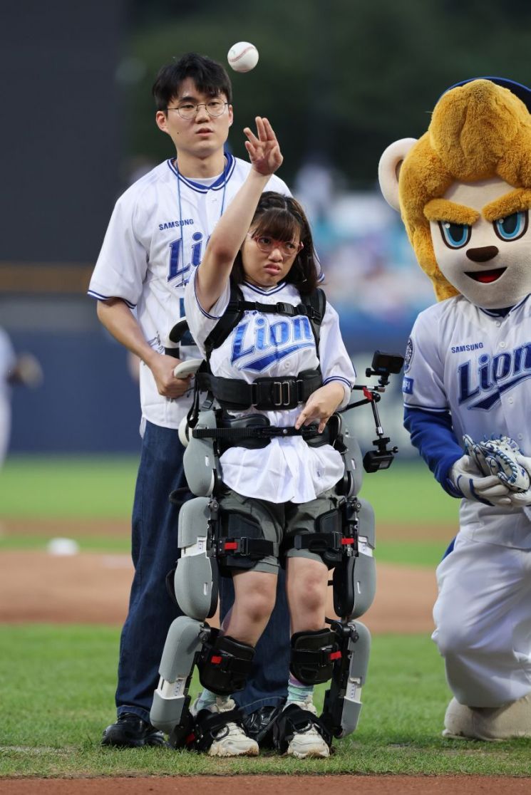 Daegu Seongbo School student Ye-won Kim, who usually relies on a wheelchair, is throwing the first pitch in a professional baseball game with the help of a walking rehabilitation robot.