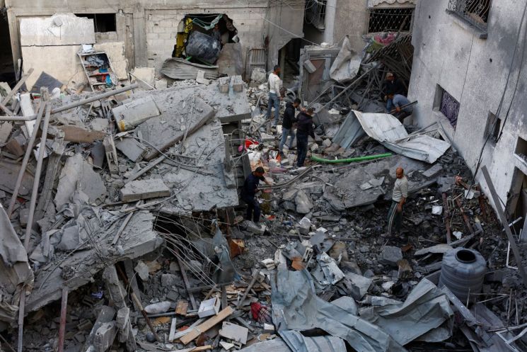 23일(현지시간) 가자지구 중부에서 주민들이 이스라엘군 공습에 파괴된 건물 잔해를 살피고 있다. 로이터·연합뉴스