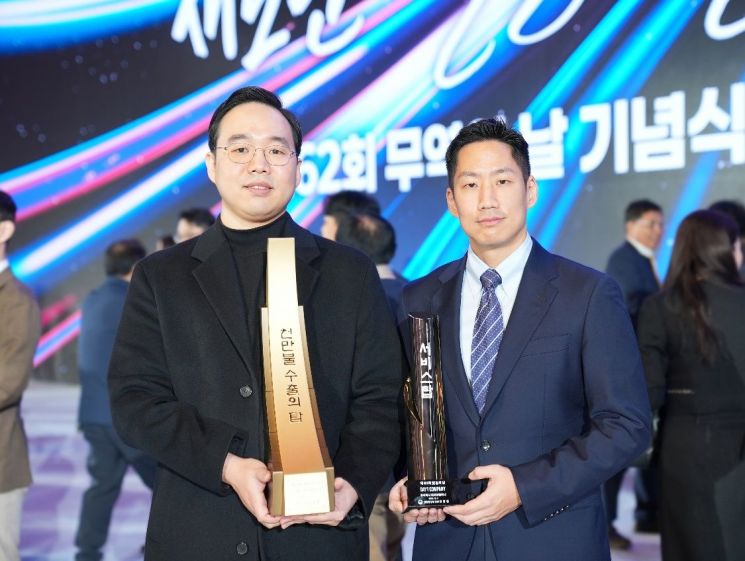 왼쪽부터 김동혁 데이원컴퍼니 콜로소 및 글로벌 부문 총괄 대표와 이강민 데이원컴퍼니 대표가 제 62회 무역의 날 기념식에서 '1000만불 수출의 탑'과 '서비스탑'을 들고 기념 촬영을 하고 있다. 데이원컴퍼니