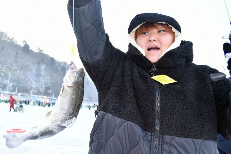 화천산천어축제장을 찾은 탐방객이 24일 낚시로 잡은 물고기를 들어 보이고 있다. 화천군 제공