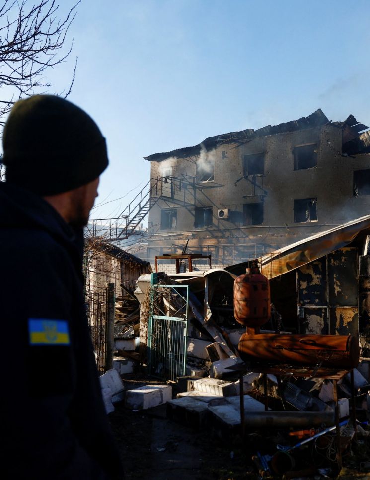 지난 14일(현지시간) 우크라이나 키이우의 한 마을에서 러시아의 공격으로 피해를 입은 건물 근처에 한 주민이 서 있다. 로이터연합뉴스