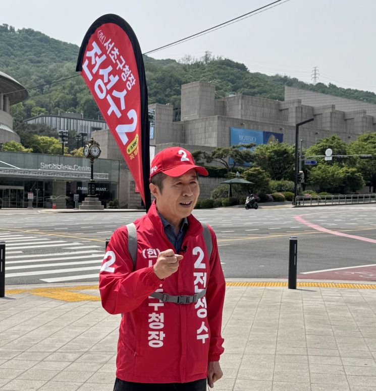 빨간 신호수 깃발을 등에 꽂은 전성수 서초구청장 후보가 예술의 전당 앞에서 주민들에게 인사하고 있다. 선거사무소 제공.