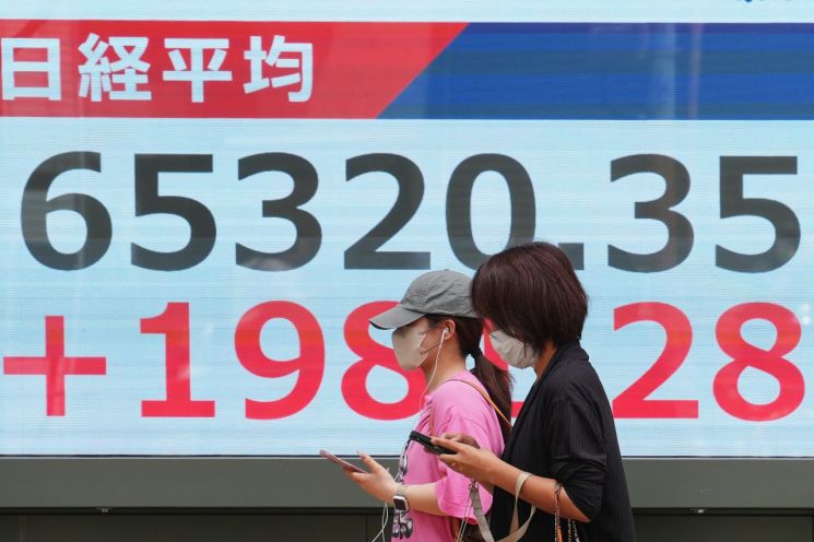 People are passing in front of the Nikkei 225 index displayed on an electronic board at a securities firm in Tokyo, Japan, on the 25th. Photo by AP