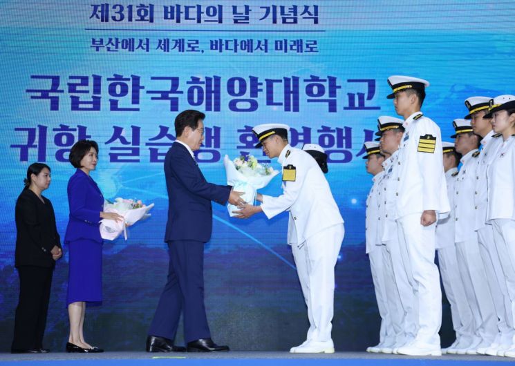 이재명 대통령이 27일 부산 영도구에서 열린 제31회 바다의 날 기념식에서 귀항 보고를 한 해양대 실습생에게 꽃다발을 주고 있다. 2026.5.27 연합뉴스