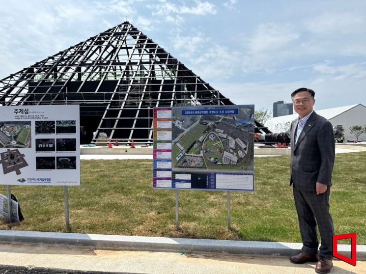 김종기 2026여수세계섬박람회 조직위원회 사무총장이 9일 전남 여수 돌산 진모지구 주행사장에서 조성 현황을 설명하고 있다. 뒤편에는 박람회 랜드마크인 피라미드형 주제관 ‘주제섬’이 공사 중이다. 김희윤 기자