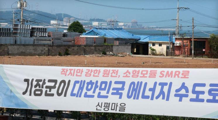 Behind the banner expressing hope for attracting SMR to Gijang-gun, Busan, which is hung along the roadside near Sinpyeong Village Hall in Gijang-gun after Korea Hydro & Nuclear Power confirmed two large nuclear power plants in Yeongdeok-gun, Gyeongbuk, and one SMR in Gijang-gun as candidate sites for new nuclear plant construction, are Kori Units 1, 2, 3, and 4. Photo by Yonhap News Agency