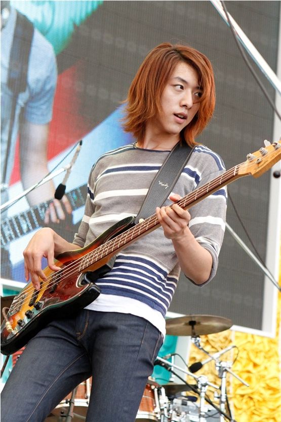 CNBLUE's bassist Lee Jung-shin, donned in a gray, blue and white striped long sleeve shirt and jeans, strums his bass during their group's performance on Mezamashi Live, hosted by Fuji TV, in Odaiba, Tokyo on August 28, 2012. [FNC Entertainment]

